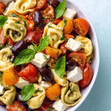 Eine Schüssel Nudeln mit Tomaten, Oliven und Käse.