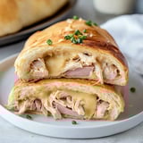 Ein Sandwich mit Hähnchen und geschmolzenem Käse auf einem weißen Teller.