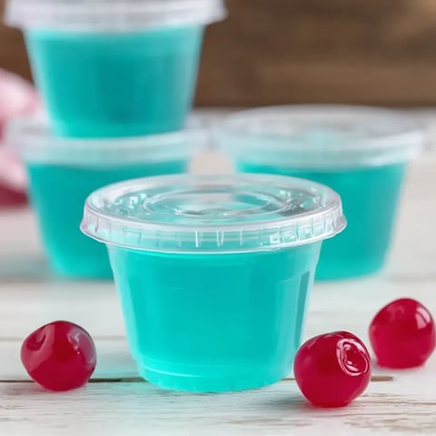 Ein Becher mit blauer Flüssigkeit und Kirschen daneben.