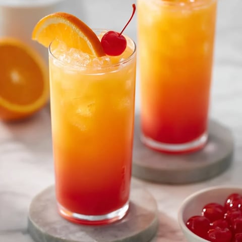 Zwei Gläser Orangensaft mit Kirschen daneben.